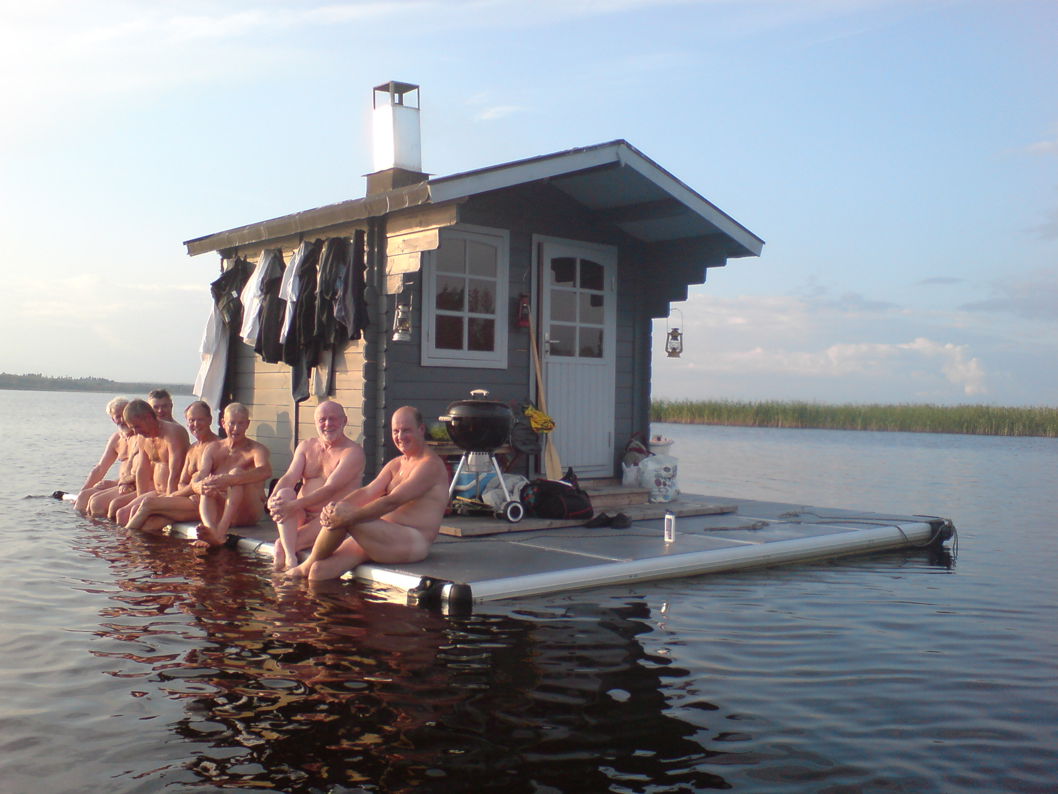 EasyFloat® bastuflotte med bastu och grill där sju personer sitter på kanten av flotten över vattnet