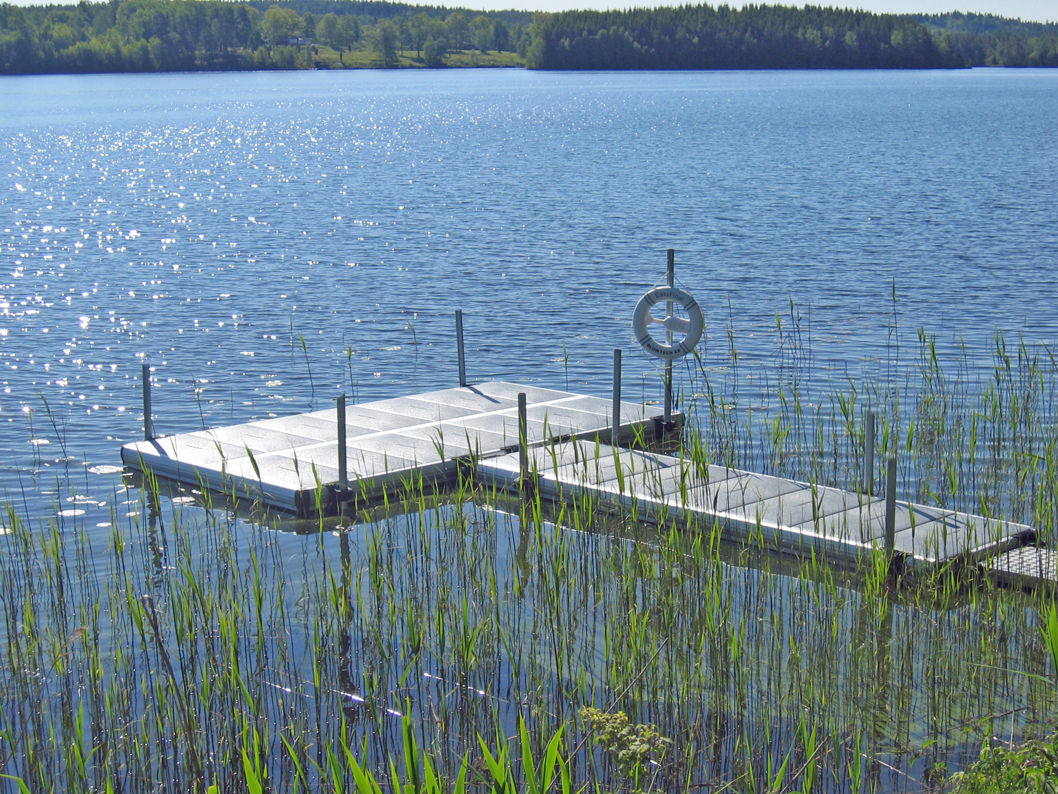 EasyFloat flytbrygga med livboj vid vass. Solen glittrar på det blå vattnet en sommardag.